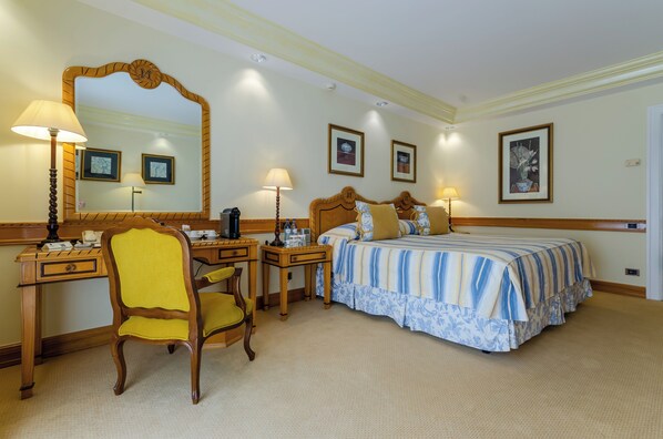 A hotel room with a bed, a desk, a chair, a mirror, and framed pictures on the wall.