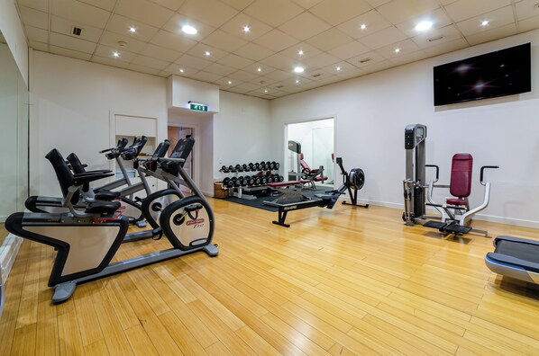 A gym with cardio machines, dumbbells, weight benches, and a rowing machine.