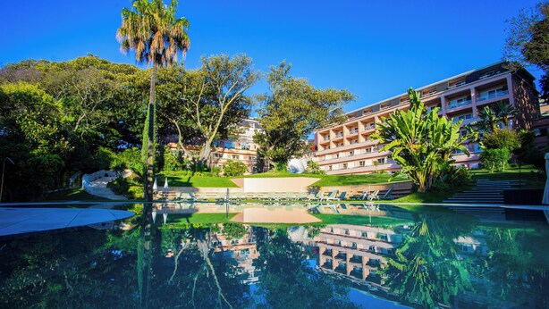 A hotel with a pool reflecting the surrounding trees and buildings, a well-maintained lawn, and a clear blue sky. - Olissippo Lapa Palace – The Leading Hotels of the World (Lisbon)
