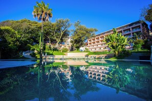 A hotel with a pool reflecting the surrounding trees and buildings, a well-maintained lawn, and a clear blue sky. - Olissippo Lapa Palace – The Leading Hotels of the World (Lisbon)