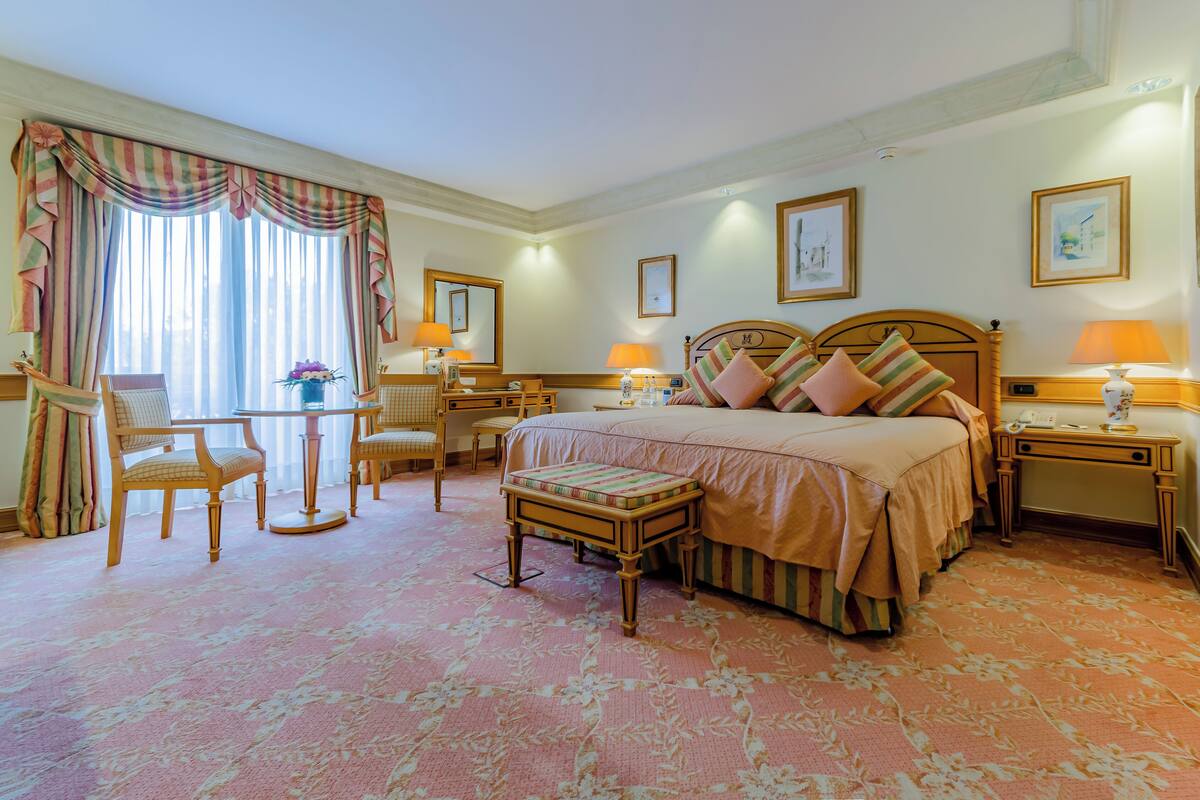 A hotel room with a large bed, two bedside tables, a desk, a chair, and a small table with a lamp.