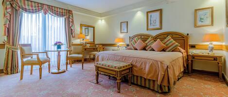 A hotel room with a large bed, two bedside tables, a desk, a chair, and a small table with a lamp.