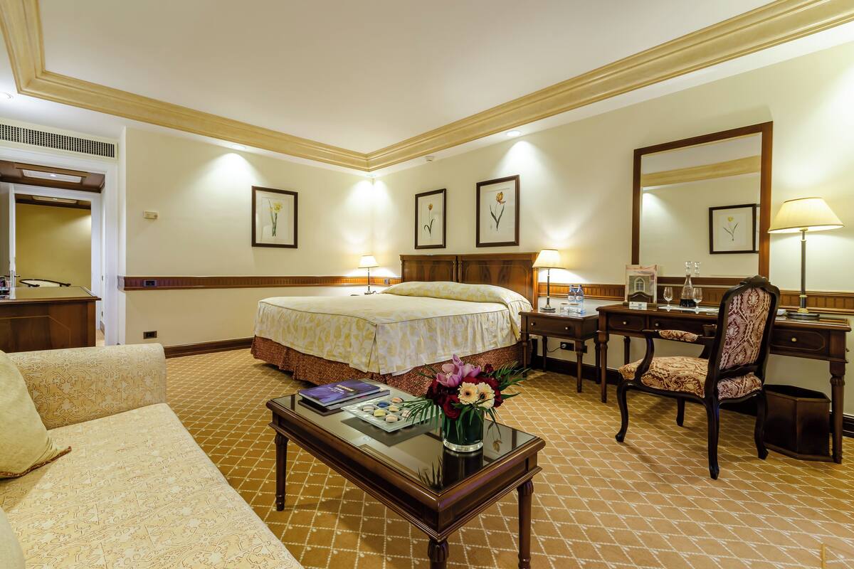 A hotel room with a bed, a desk, a chair, a coffee table, and a mirror.