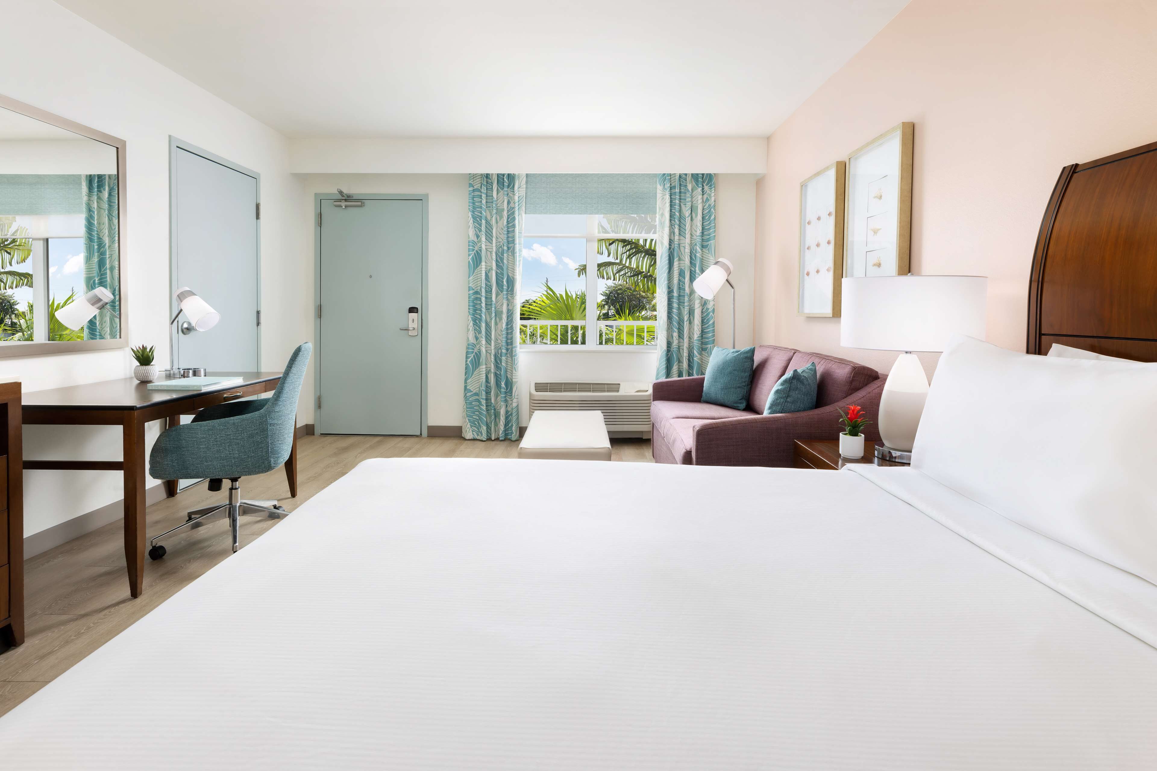 Une chambre d’hôtel comprenant un lit, un bureau, une chaise, un canapé et un balcon avec des rideaux.