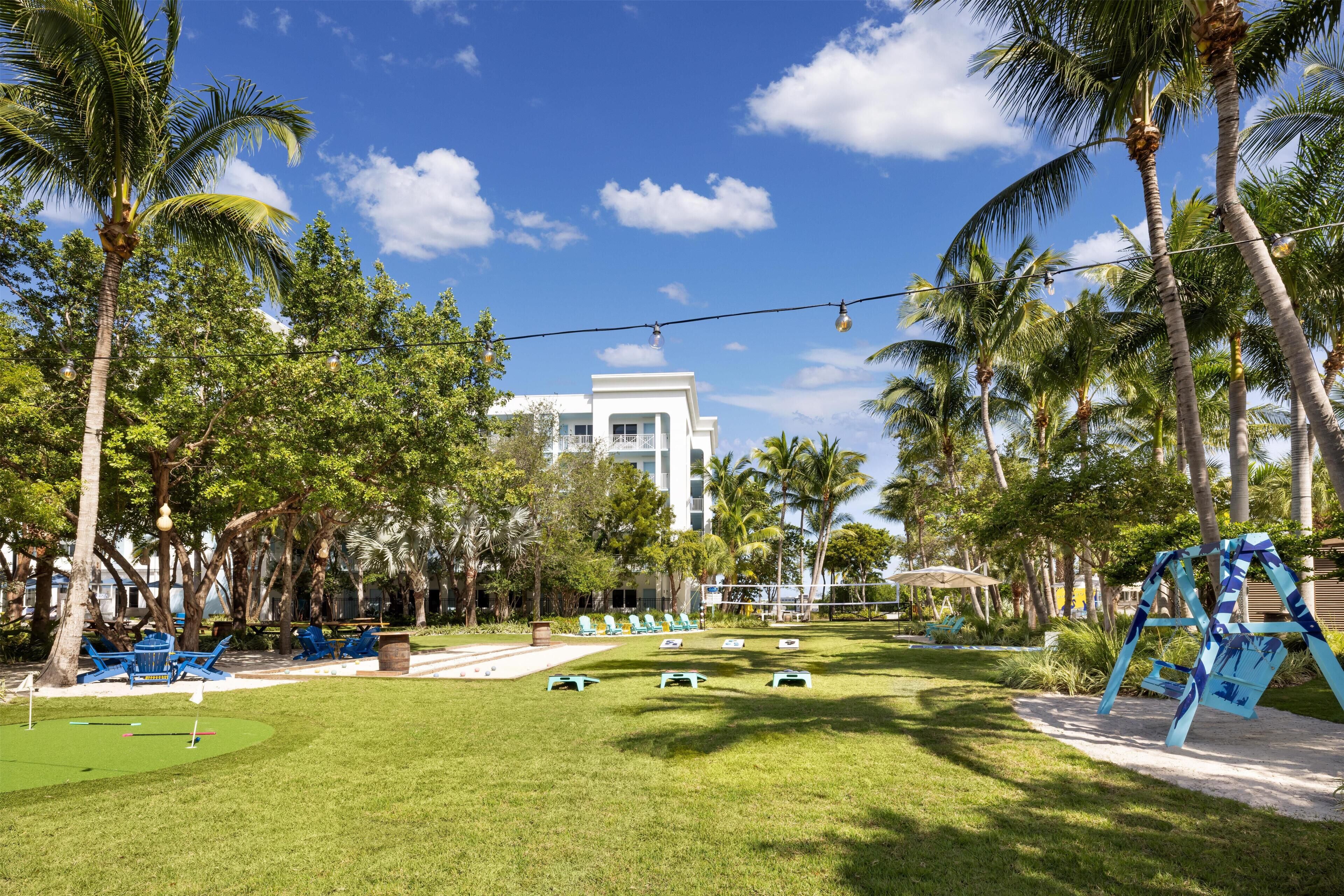 A golf course with a putting green, lounge chairs, and palm trees.