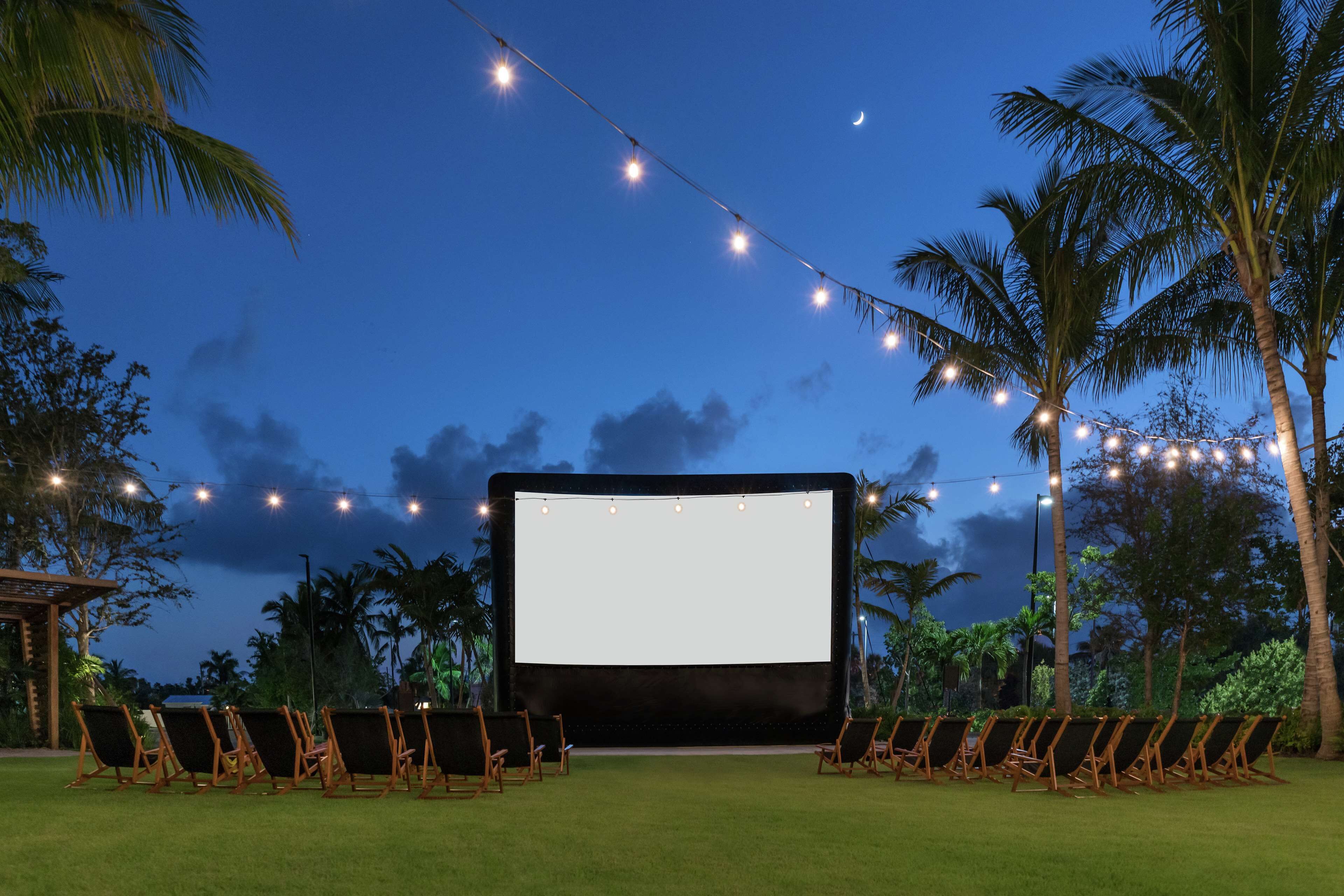 Una pantalla de cine al aire libre con filas de sillas y luces de cadena contra un cielo nocturno.