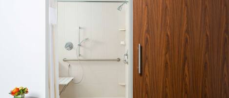A bathroom with a shower, a wooden door, and a small table with a vase.