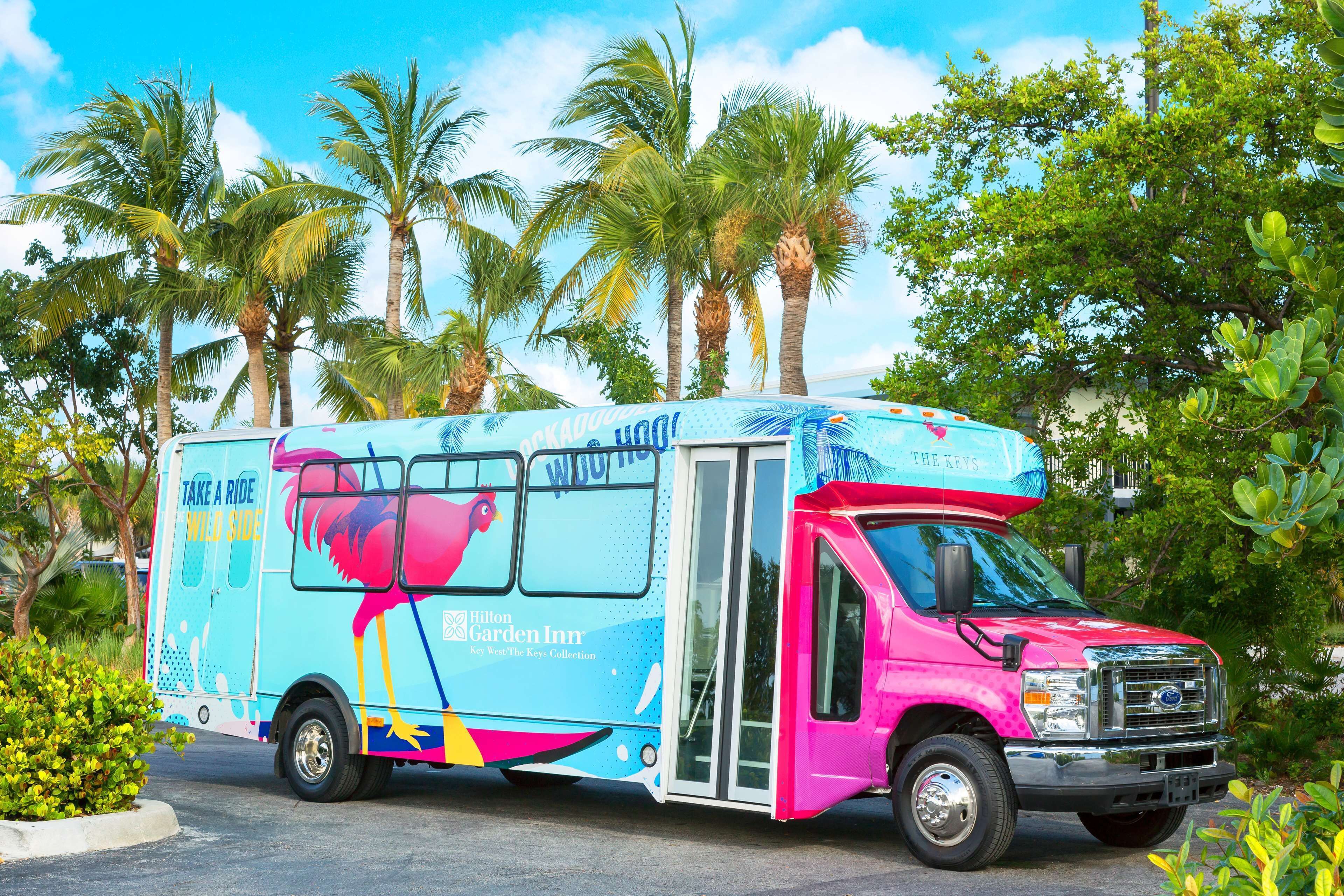 A colorful food truck with a tropical design, parked in a lush, green area with palm trees.
