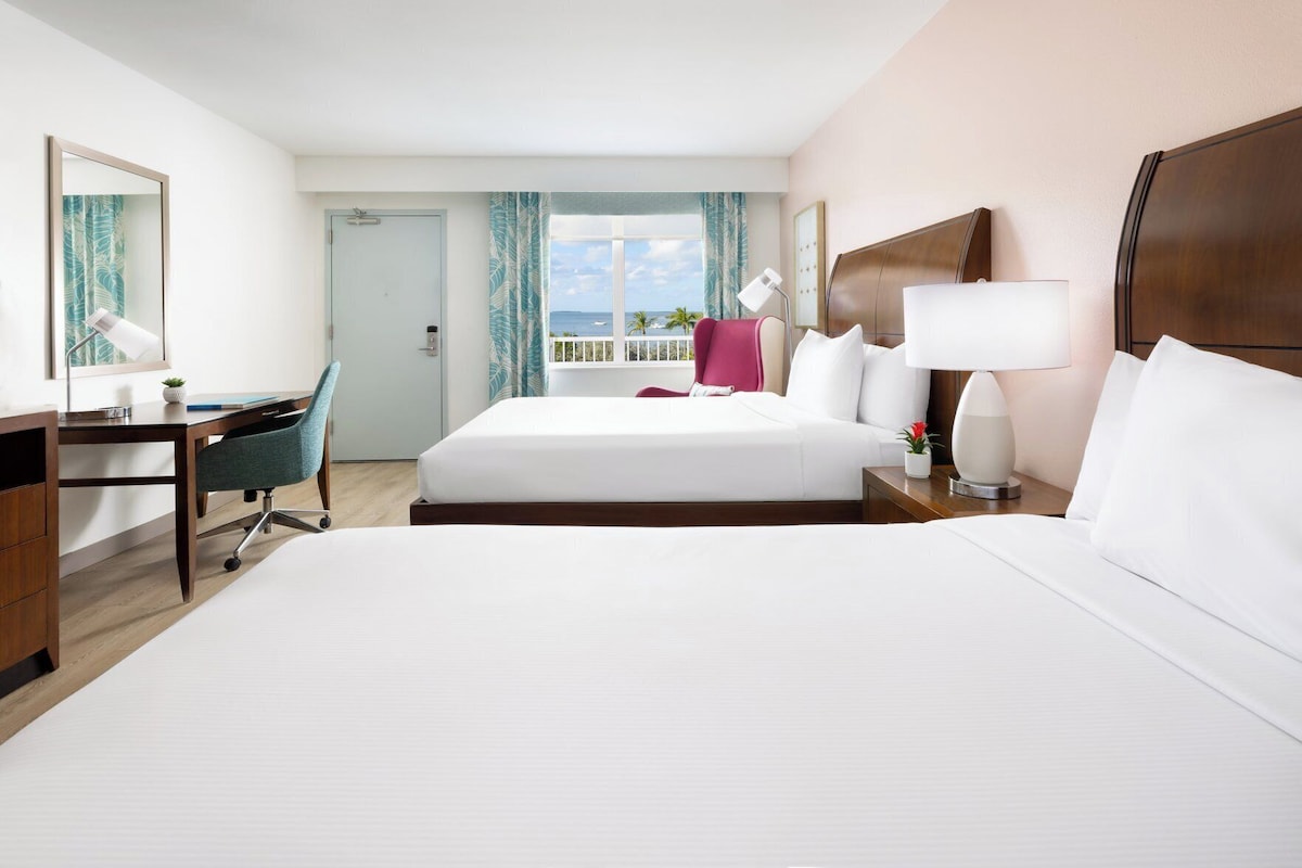 Habitación de hotel con cama, escritorio, silla y vista al océano.