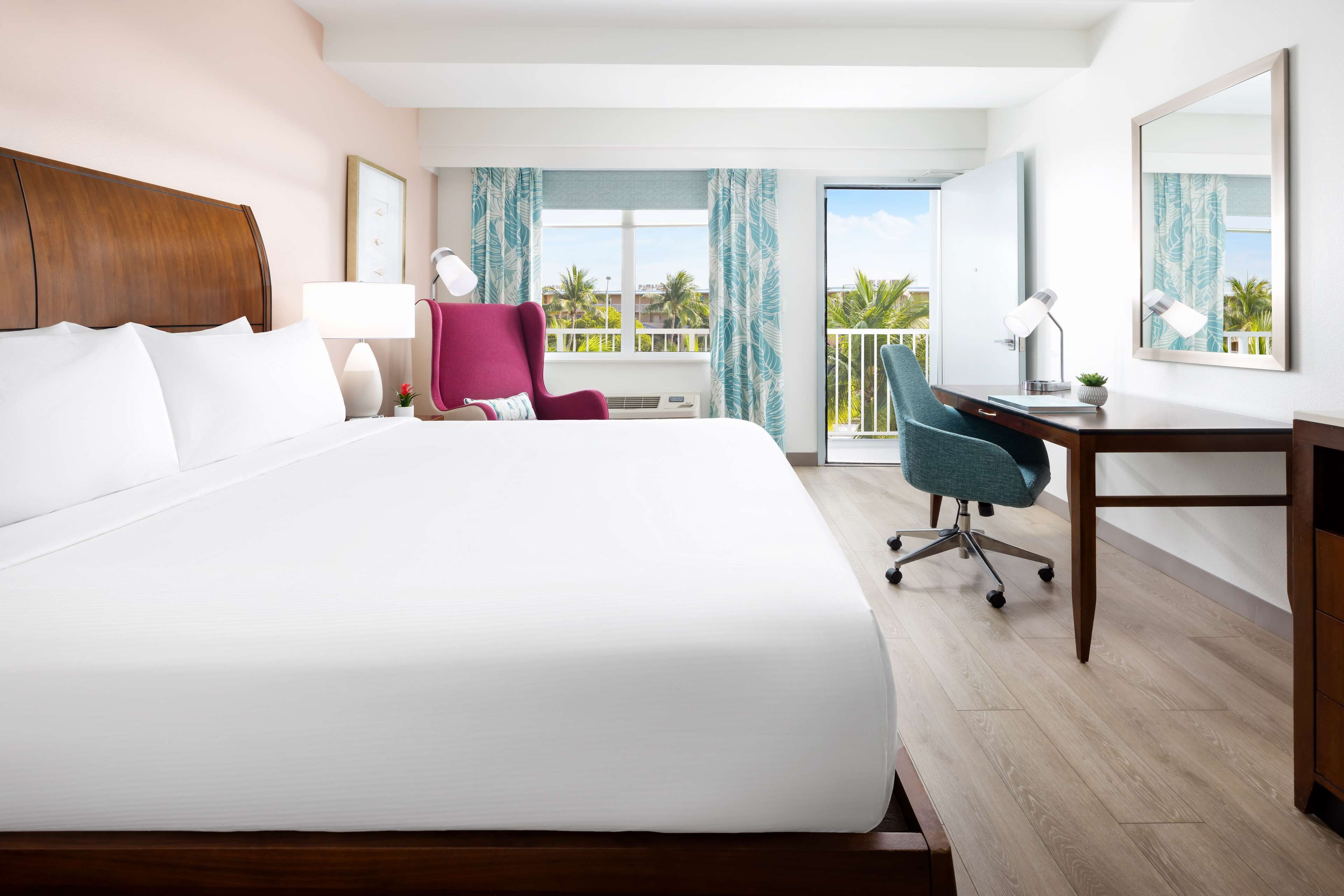 Habitación de hotel con una cama grande, un escritorio, una silla, una lámpara y vistas al exterior.