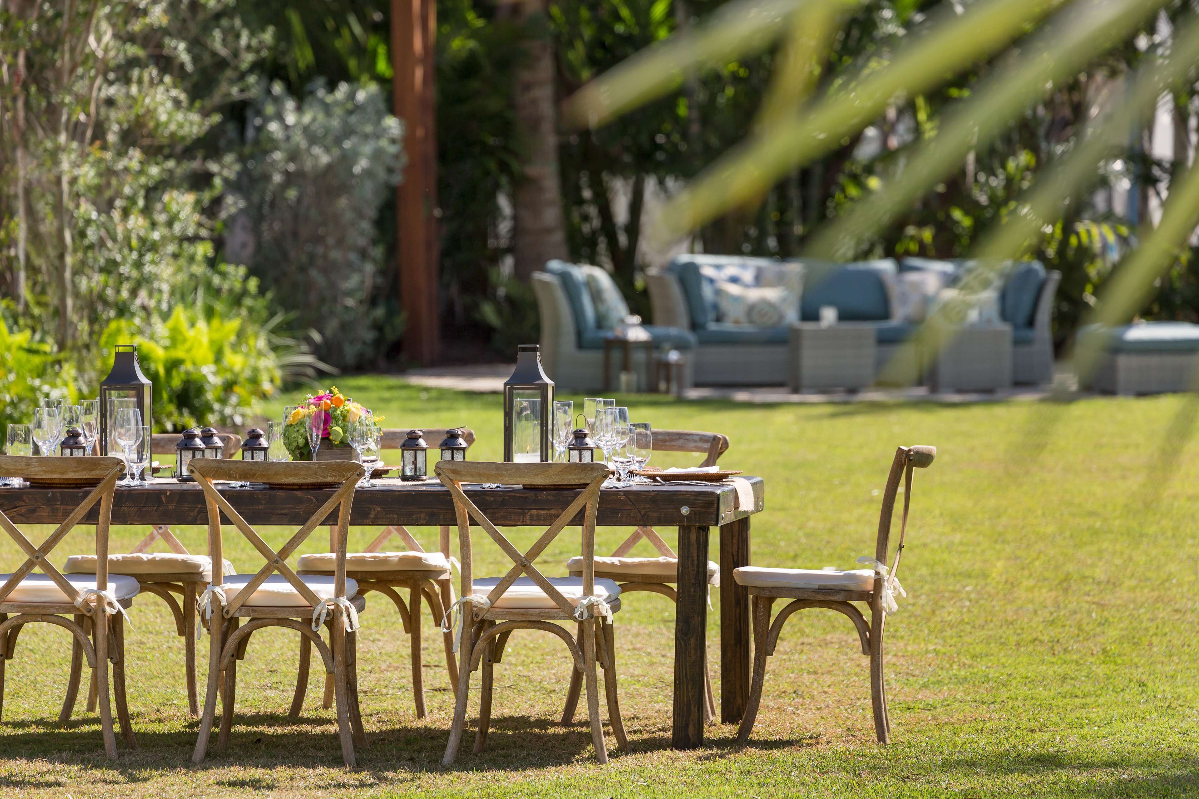 An outdoor dining area with a wooden table and chairs, surrounded by lush greenery and a seating area with sofas and chairs.