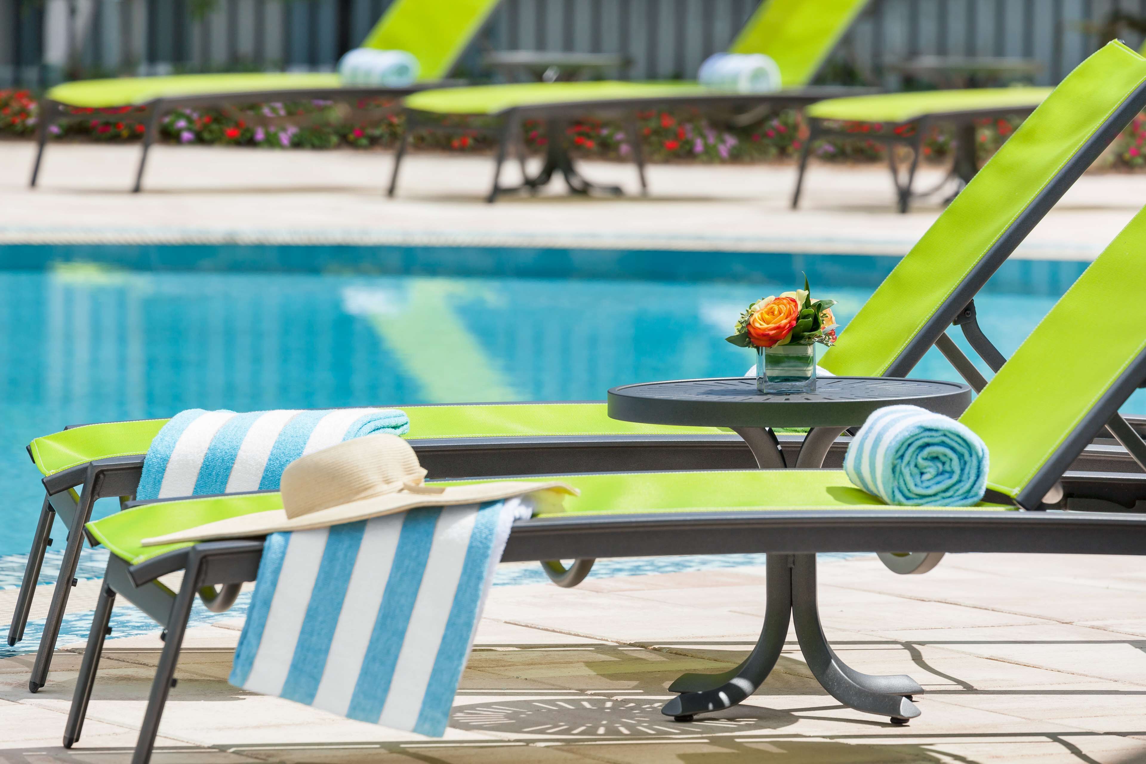 Zona de piscina amb gandules, una taula petita amb un vas de flors i una tovallola enrotllada.