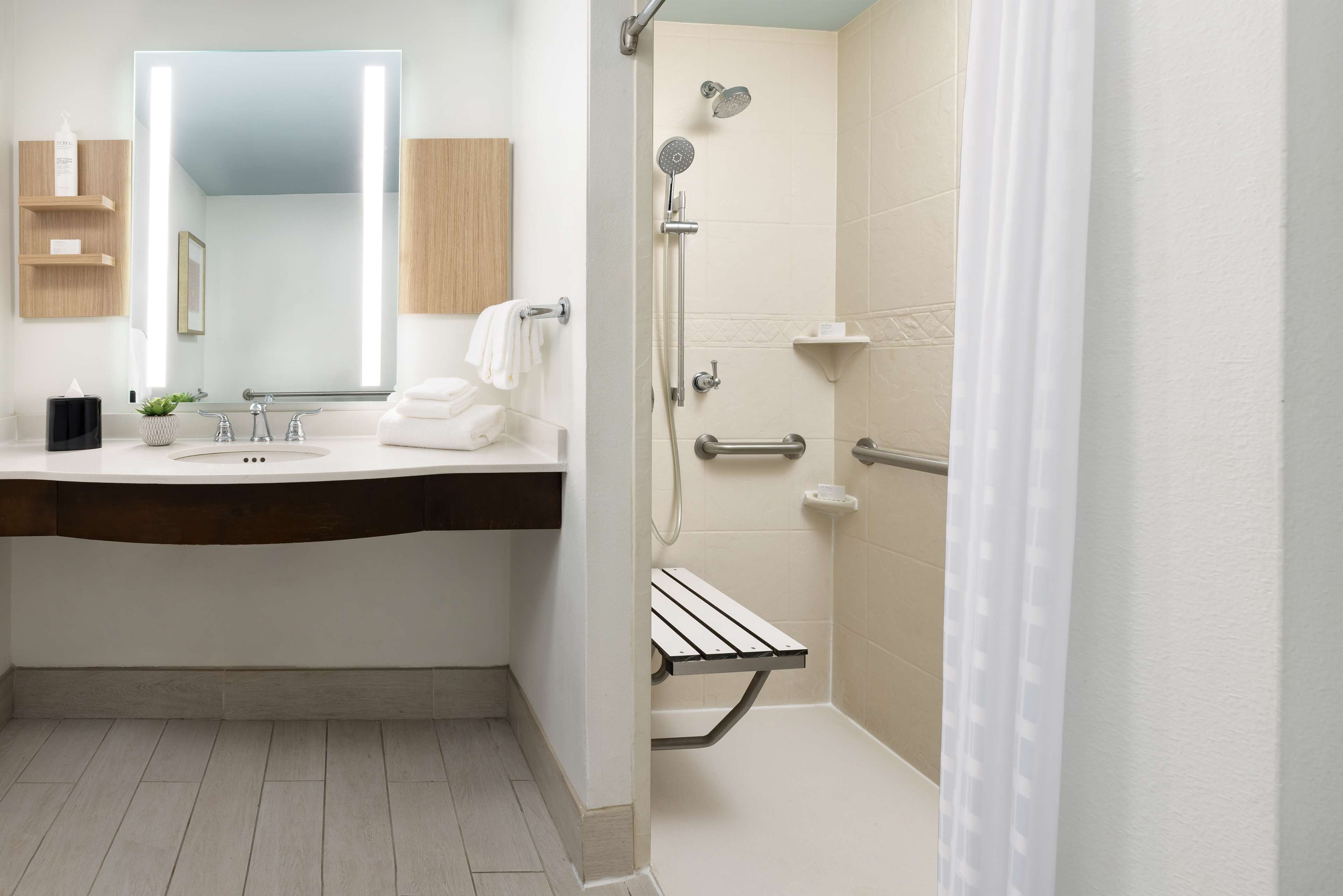 A modern bathroom with a large mirror, a sink, a shower with a handheld showerhead, and a towel rack.