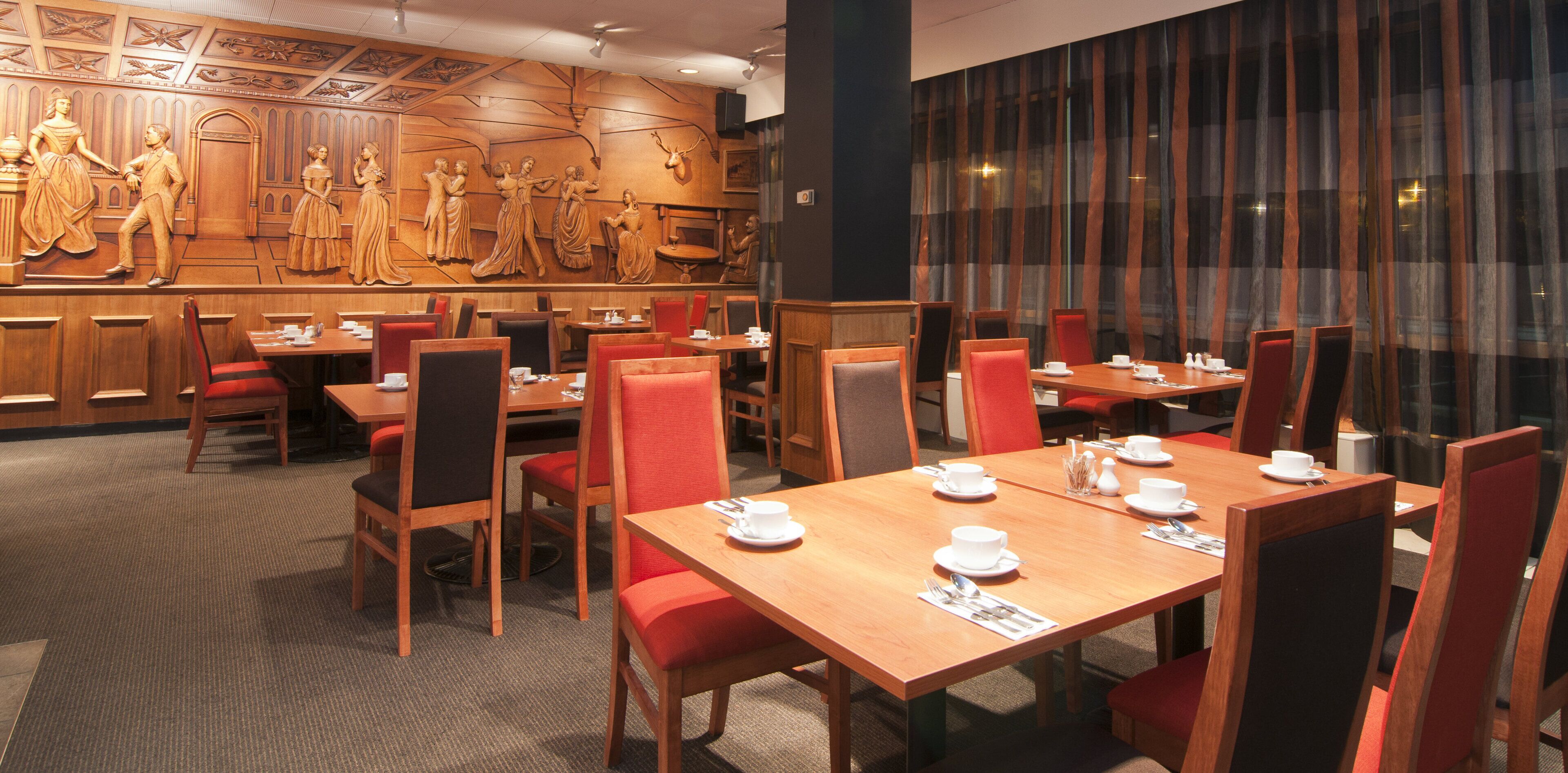 A restaurant with wooden paneling, red chairs, and tables set for dining.