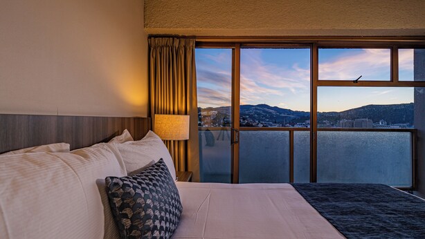 A hotel room with a large bed, a view of a body of water, and a cityscape in the background. - Kingsgate Hotel Dunedin (Dunedin)