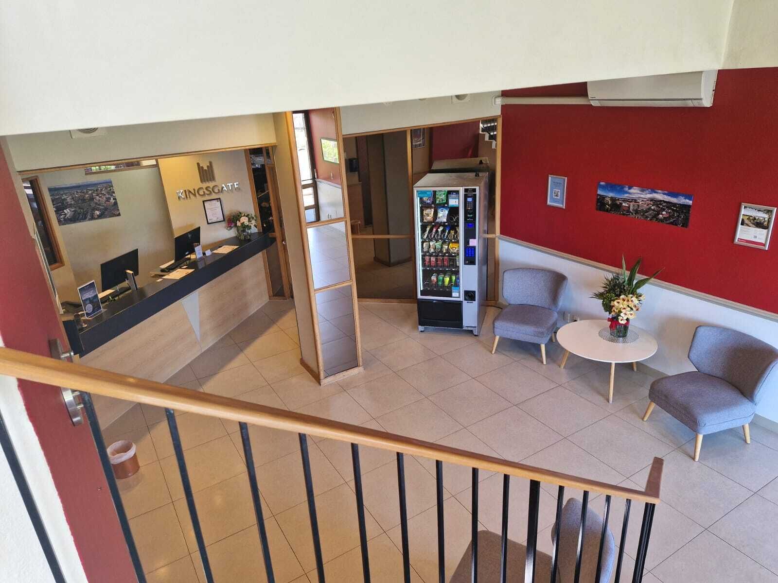 Vestíbulo de hotel con mostrador de recepción, máquina expendedora, zona de estar y una escalera.
