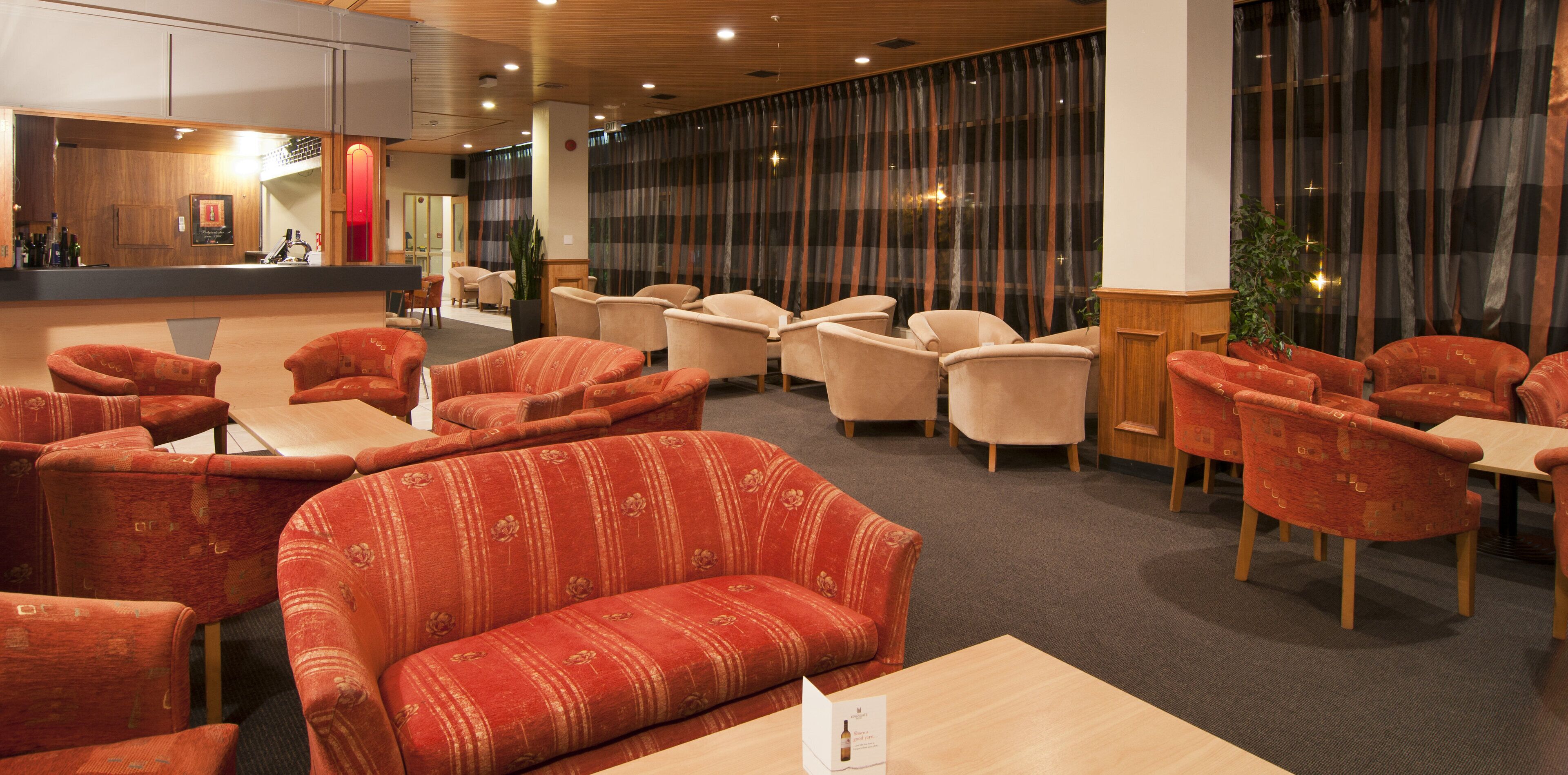 A hotel lobby with seating areas, a reception desk, and a bar.