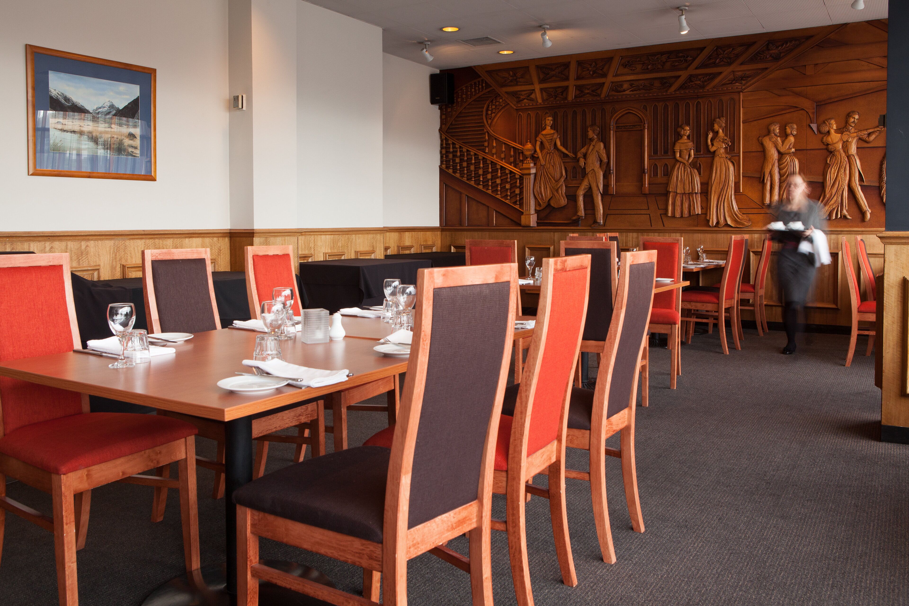 Un restaurant avec des tables et des chaises en bois, une fresque murale et un escalier.