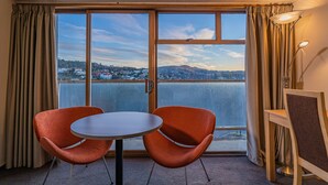 A room with a large window, two orange chairs, a small table, and a lamp. - Kingsgate Hotel Dunedin (Dunedin)