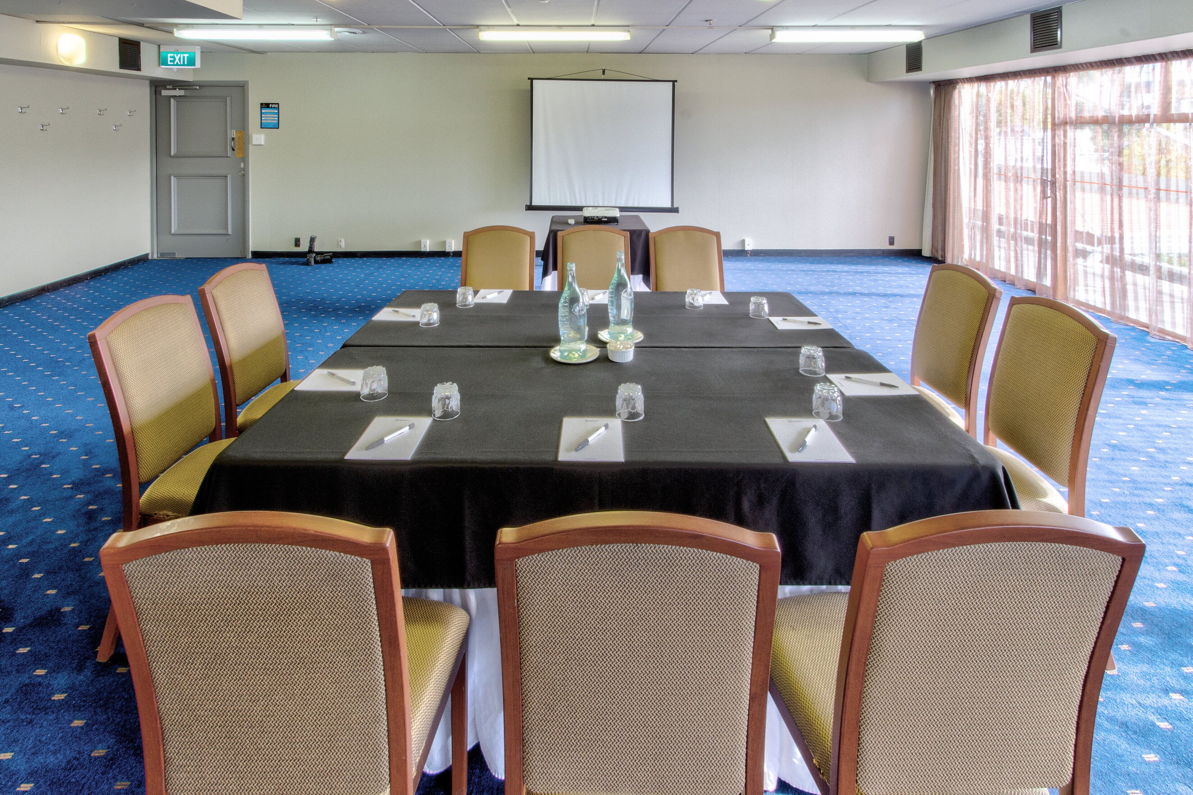A conference room with a long table, six chairs, and a projector screen.