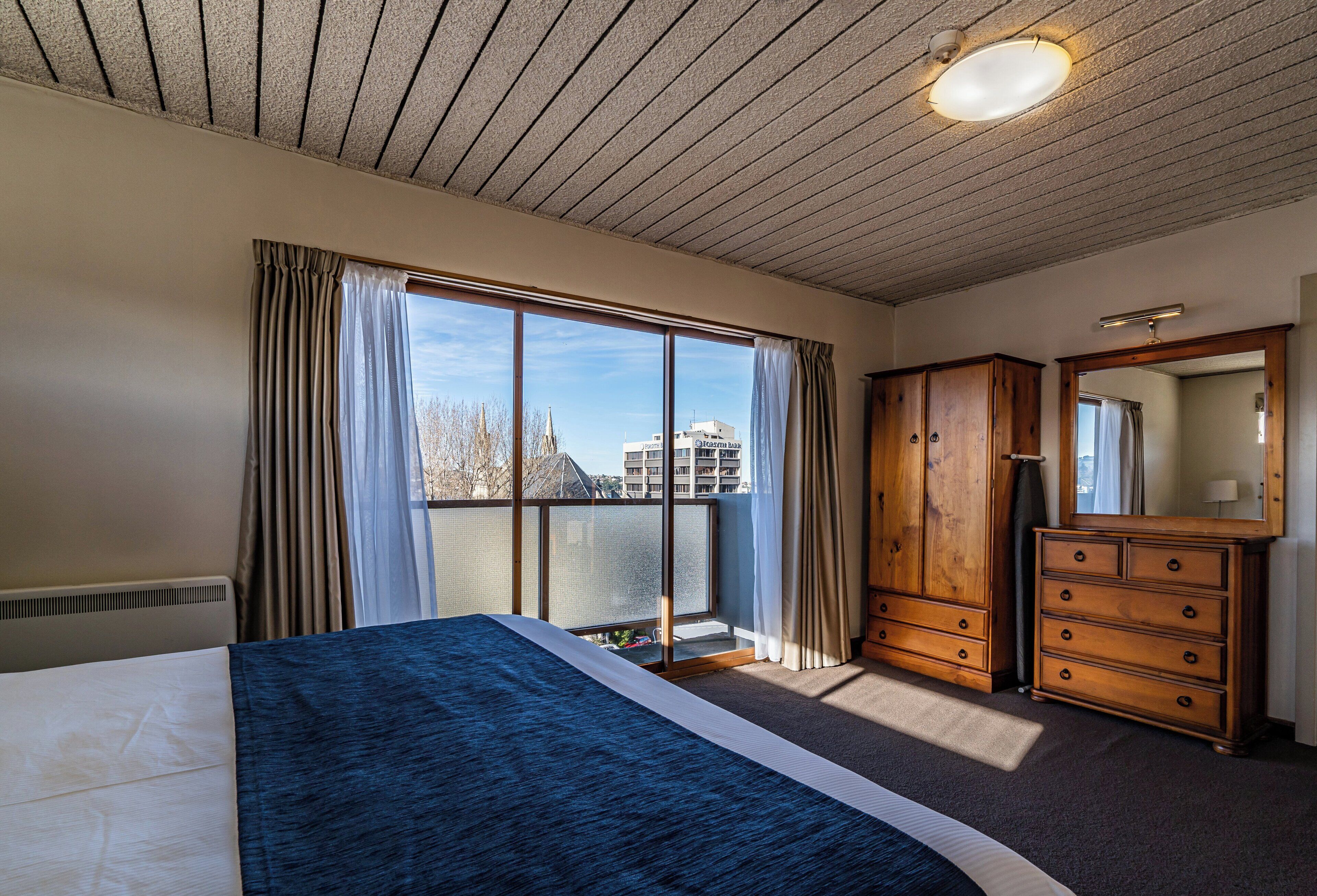A bedroom with a large bed, a dresser, a mirror, and a window with curtains.