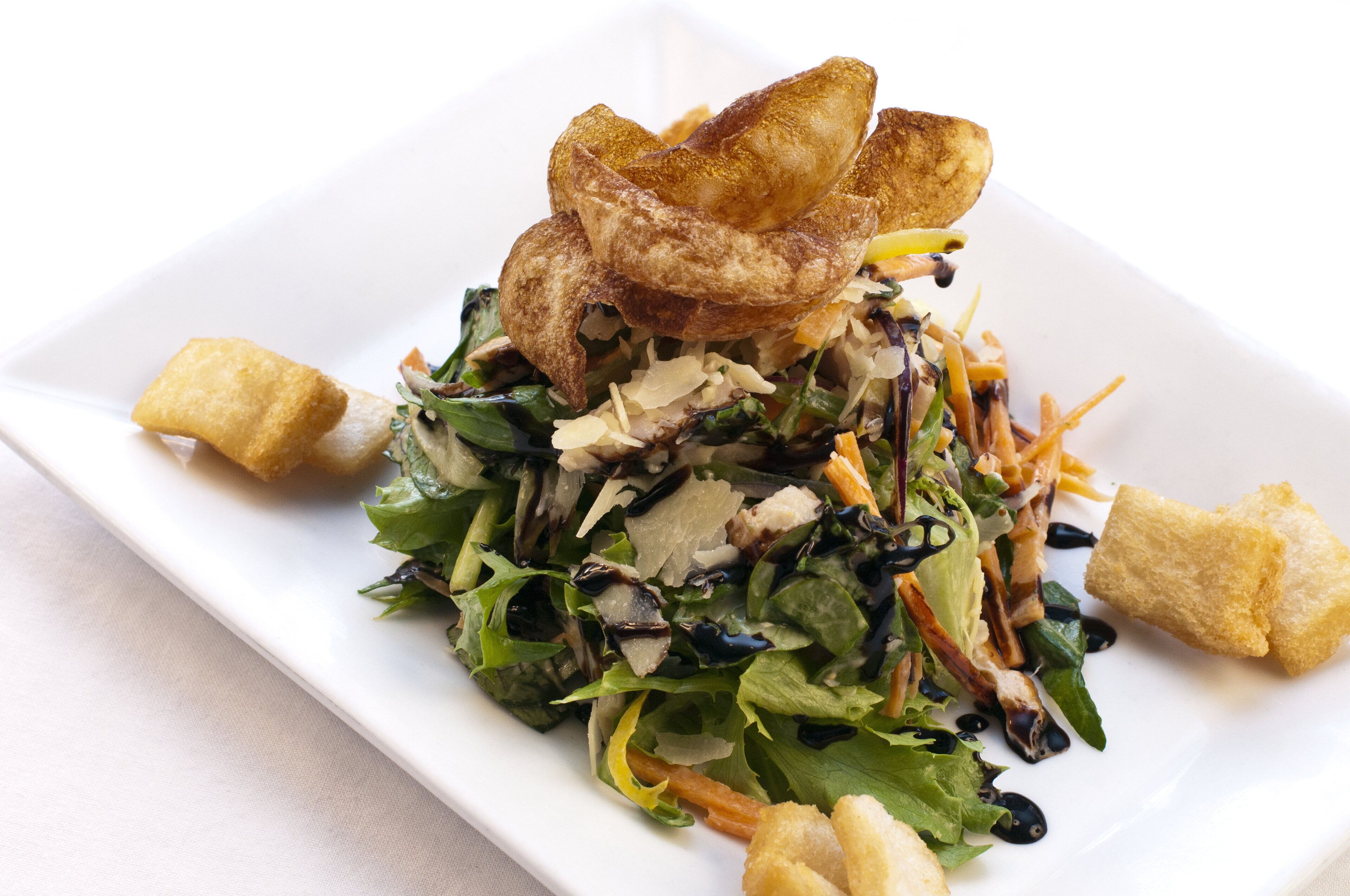 A white rectangular plate with a salad, croutons, and fried items.