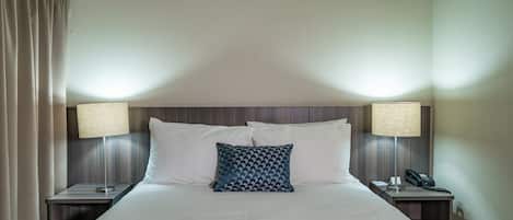 A hotel room with a large bed, two bedside tables, a patterned pillow, and a blue throw blanket.