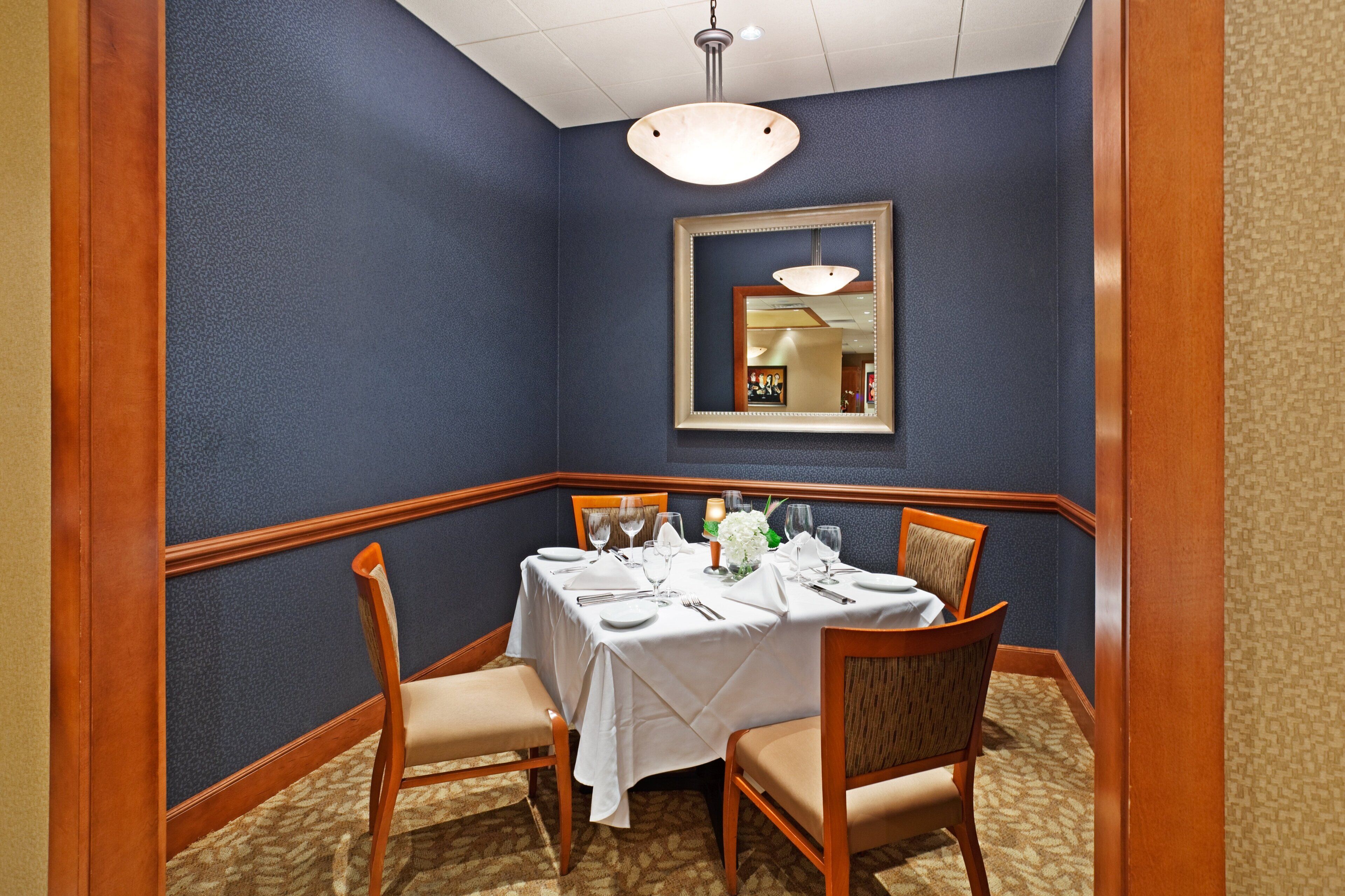 A dining area with a table set for four, chairs, a mirror, and a hanging light fixture.