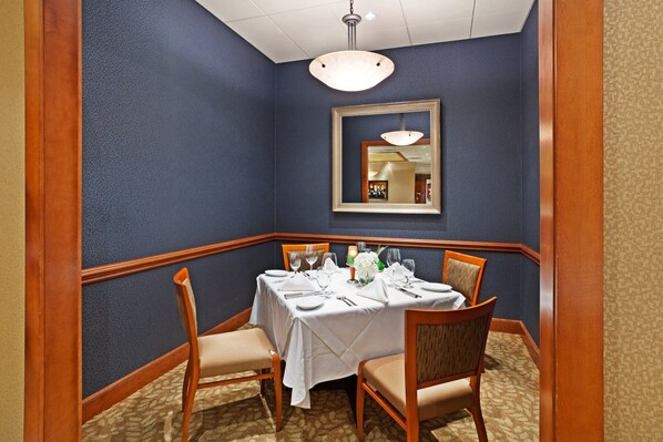 A dining area with a table set for four, chairs, a mirror, and a hanging light fixture.