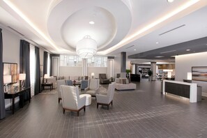 Un hall d’entrée spacieux au design moderne, comprenant un comptoir d’accueil, un espace détente avec des canapés et des fauteuils, et un grand lustre.