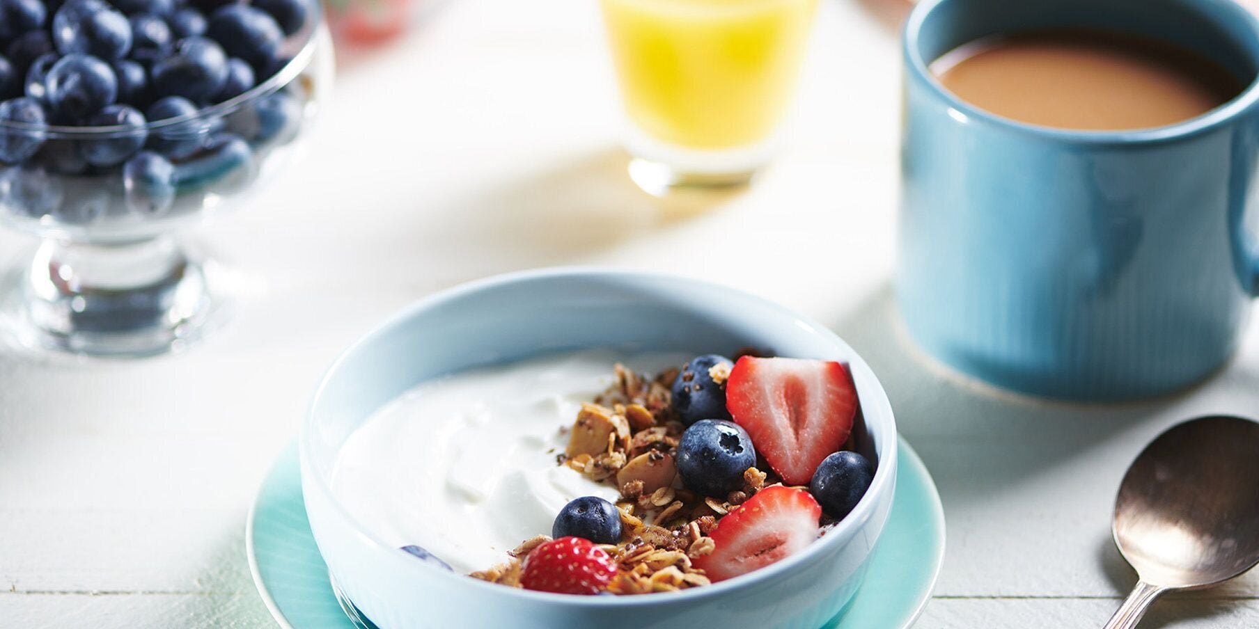 A bowl of yogurt with granola and berries, a cup of coffee, and a glass of orange juice on a table.