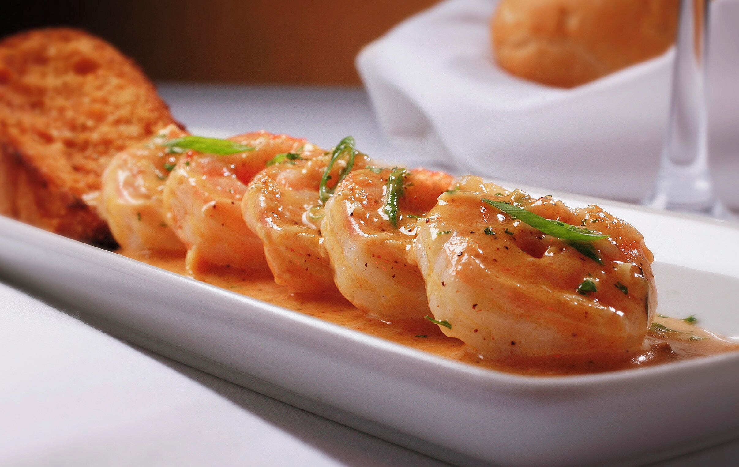 A plate of shrimp with a sauce, garnished with herbs, and a piece of bread on the side.