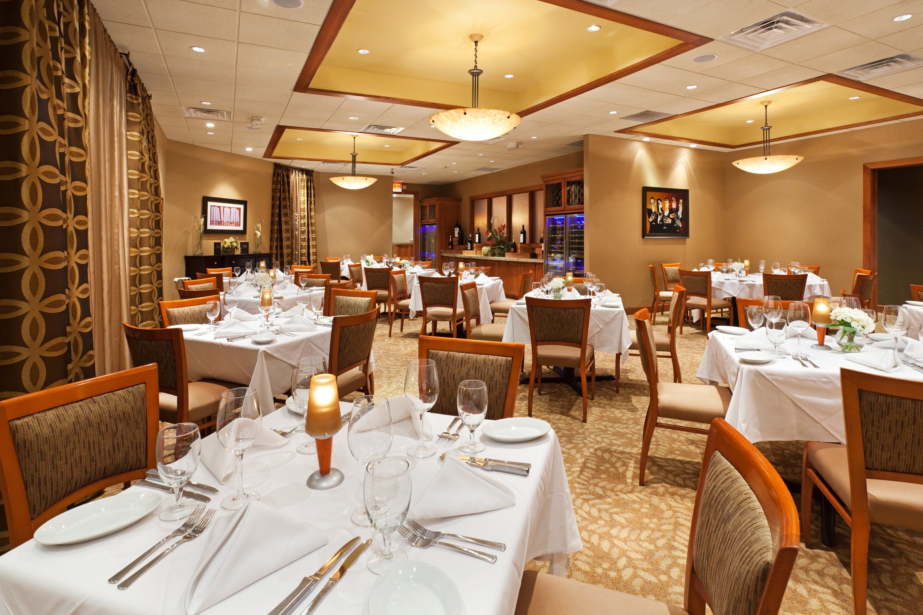 Un comedor de hotel con varias mesas dispuestas para los huéspedes, con manteles blancos, sillas y cristalería.