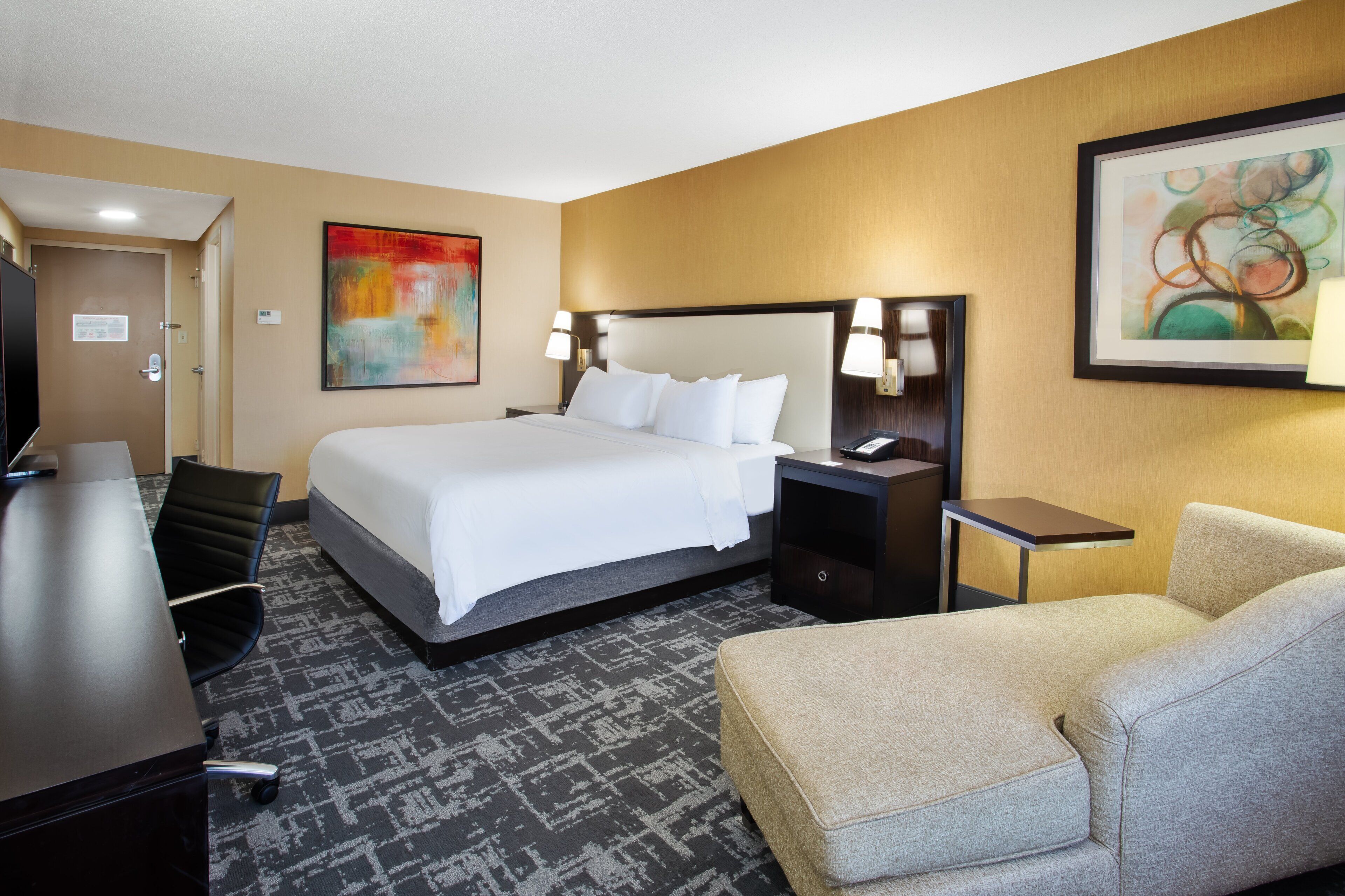 A hotel room with a large bed, a desk, a chair, and two nightstands with lamps.