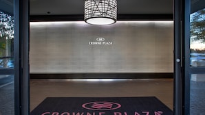 L’entrée d’un hôtel, avec un paillasson portant l’inscription « Crowne Plaza Greenville » et un logo affiché sur le mur.