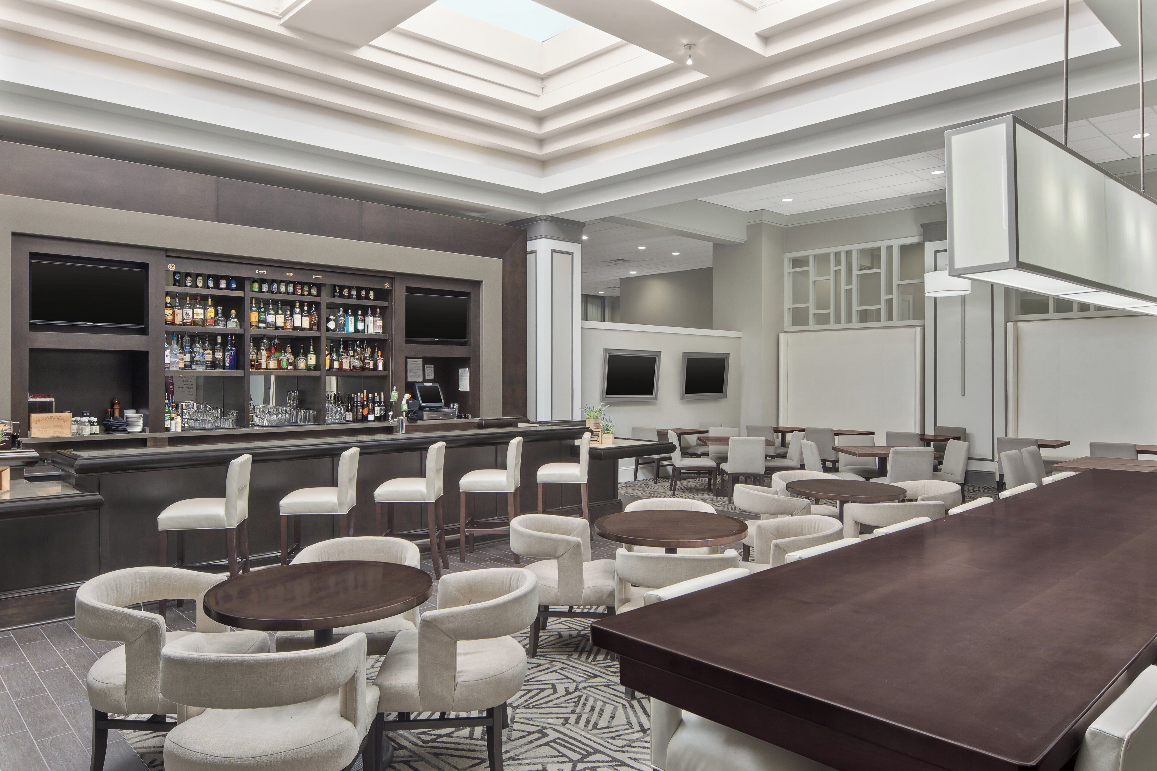A modern bar area with a long counter, multiple seating options including bar stools and round tables, and a patterned floor.