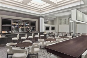 A modern bar area with a long counter, multiple seating options including bar stools and round tables, and a patterned floor.