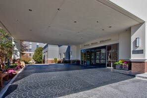 A hotel entrance with a welcoming sign, a covered walkway, and a landscaped area with benches and flowers. - Crowne Plaza Hotel Greenville-I-385-Roper Mtn Rd by IHG (Greenville)
