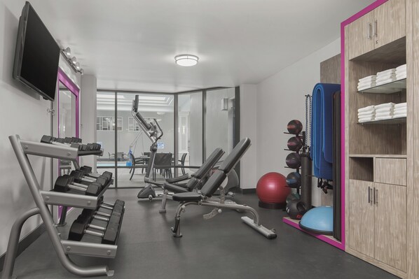 Gimnasio con equipo de ejercicio, televisor y zona de taquillas.