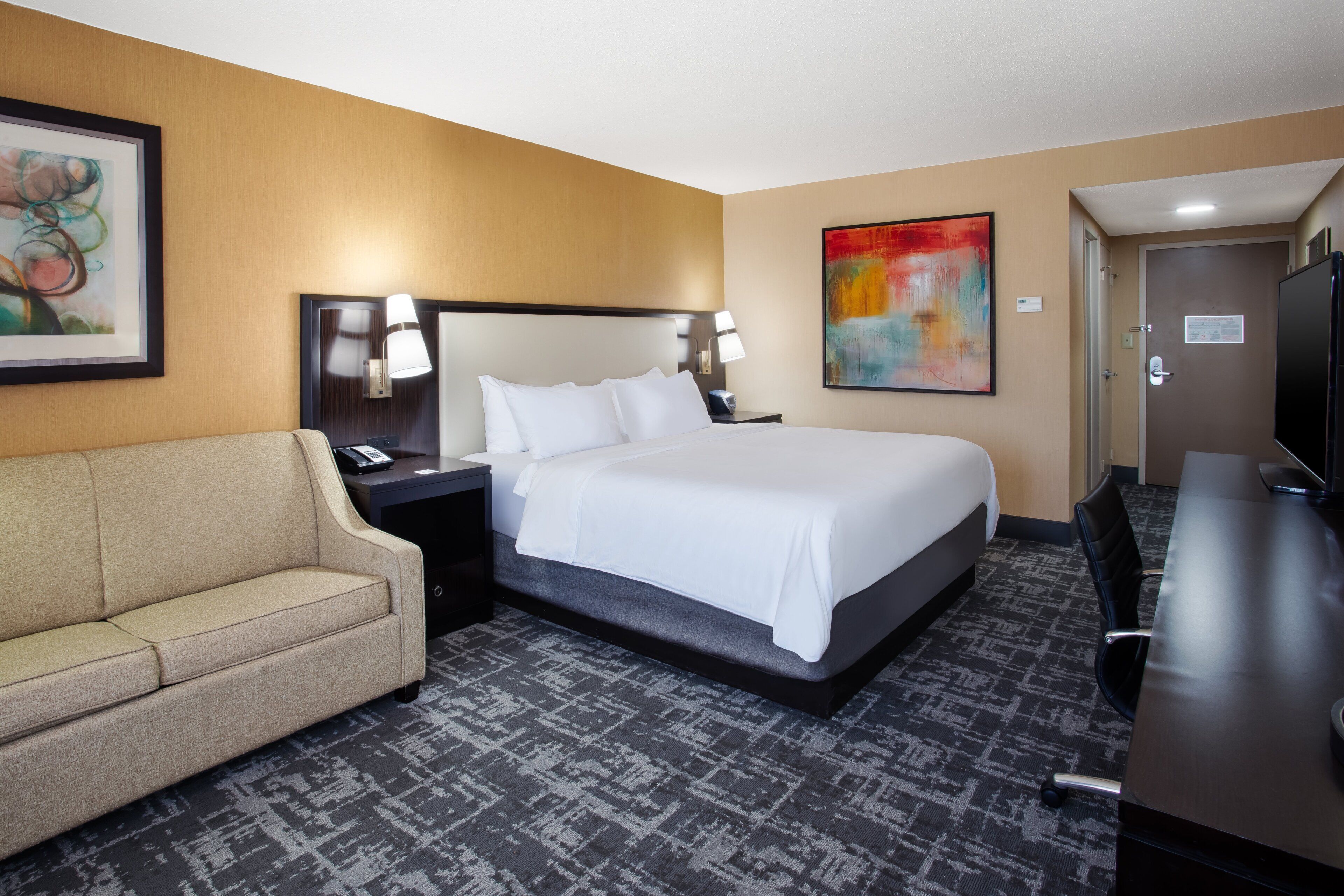A hotel room with a bed, a sofa, a desk, and a TV.