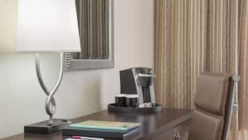 Habitación de hotel con escritorio, lámpara, cafetera, silla y espejo.