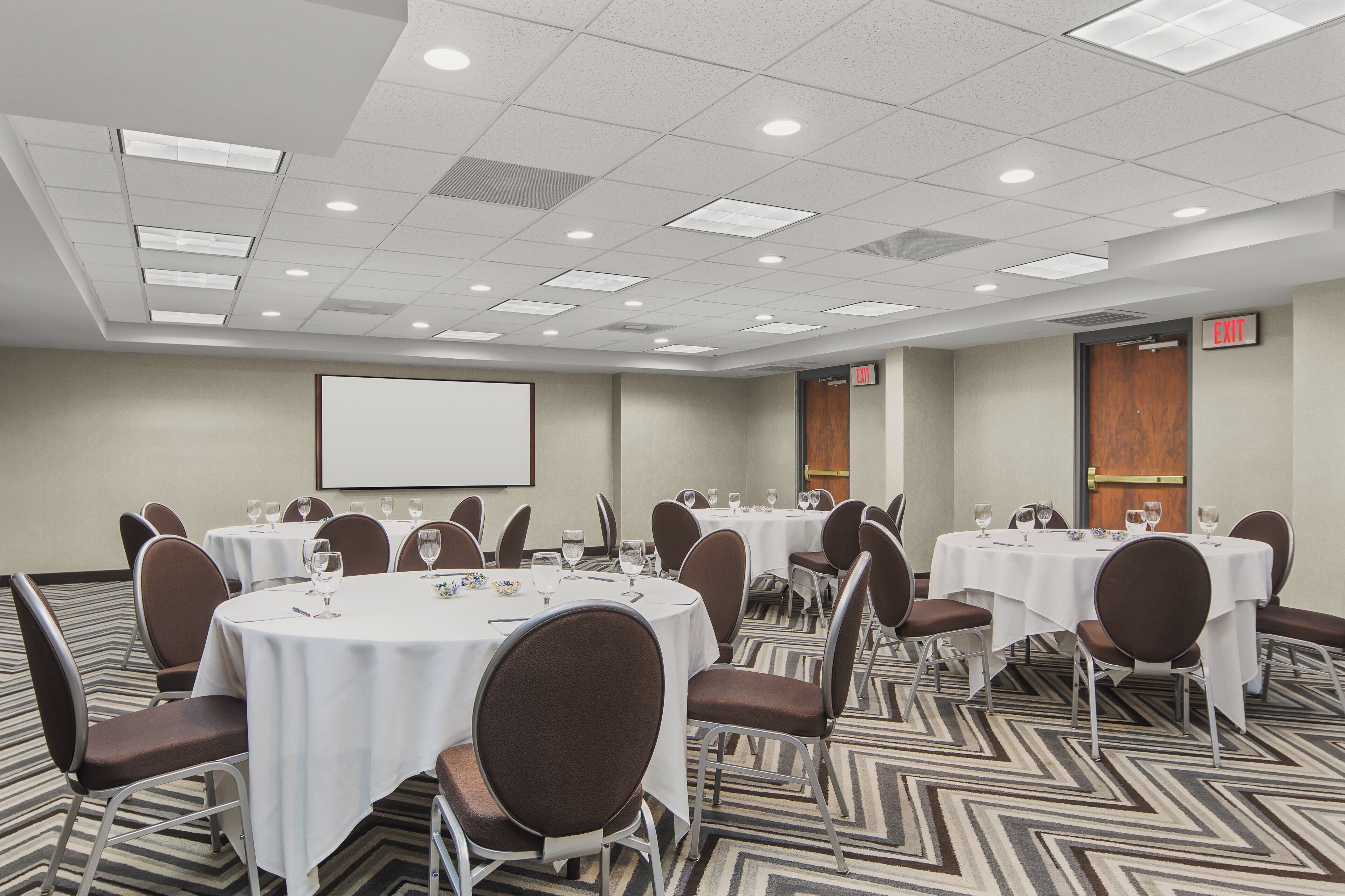 A conference room with multiple tables, chairs, and a projection screen.