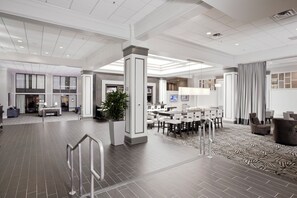 A spacious hotel lobby with a reception desk, seating area, and a large plant.