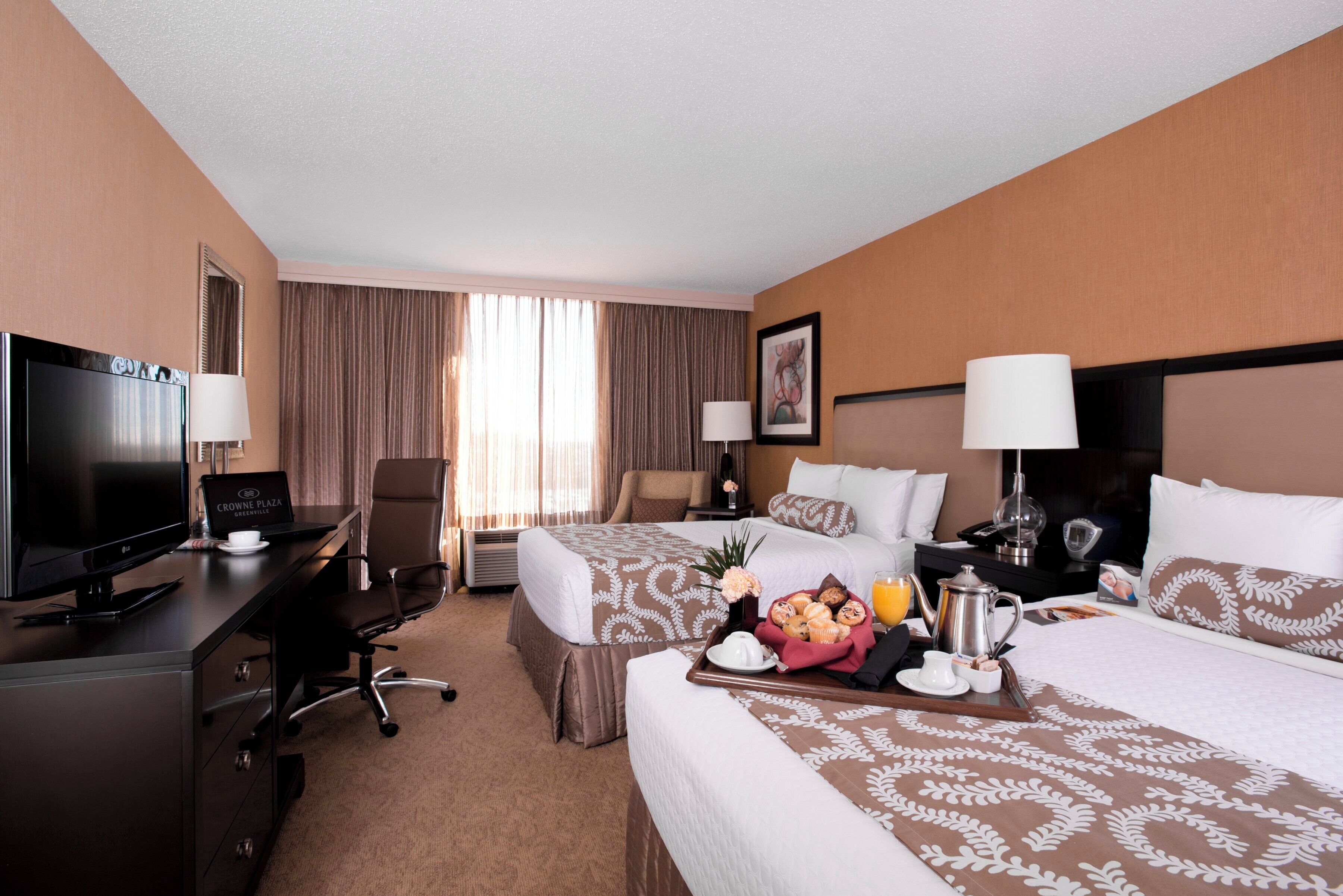 A hotel room with a desk, two beds, a TV, and a breakfast tray.