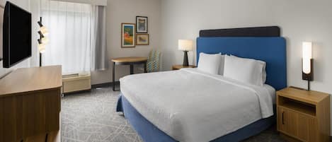 A hotel room with a bed, bedside tables, a desk, a chair, a TV, and artwork on the wall.