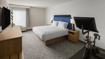 Una habitación de hotel con cama, escritorio, televisor, bicicleta y ventana con cortinas.