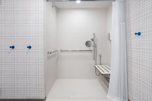 Un baño pequeño con revestimiento de azulejos blancos, un cabezal de ducha de mano, un perchero y un panel de control de la ducha.