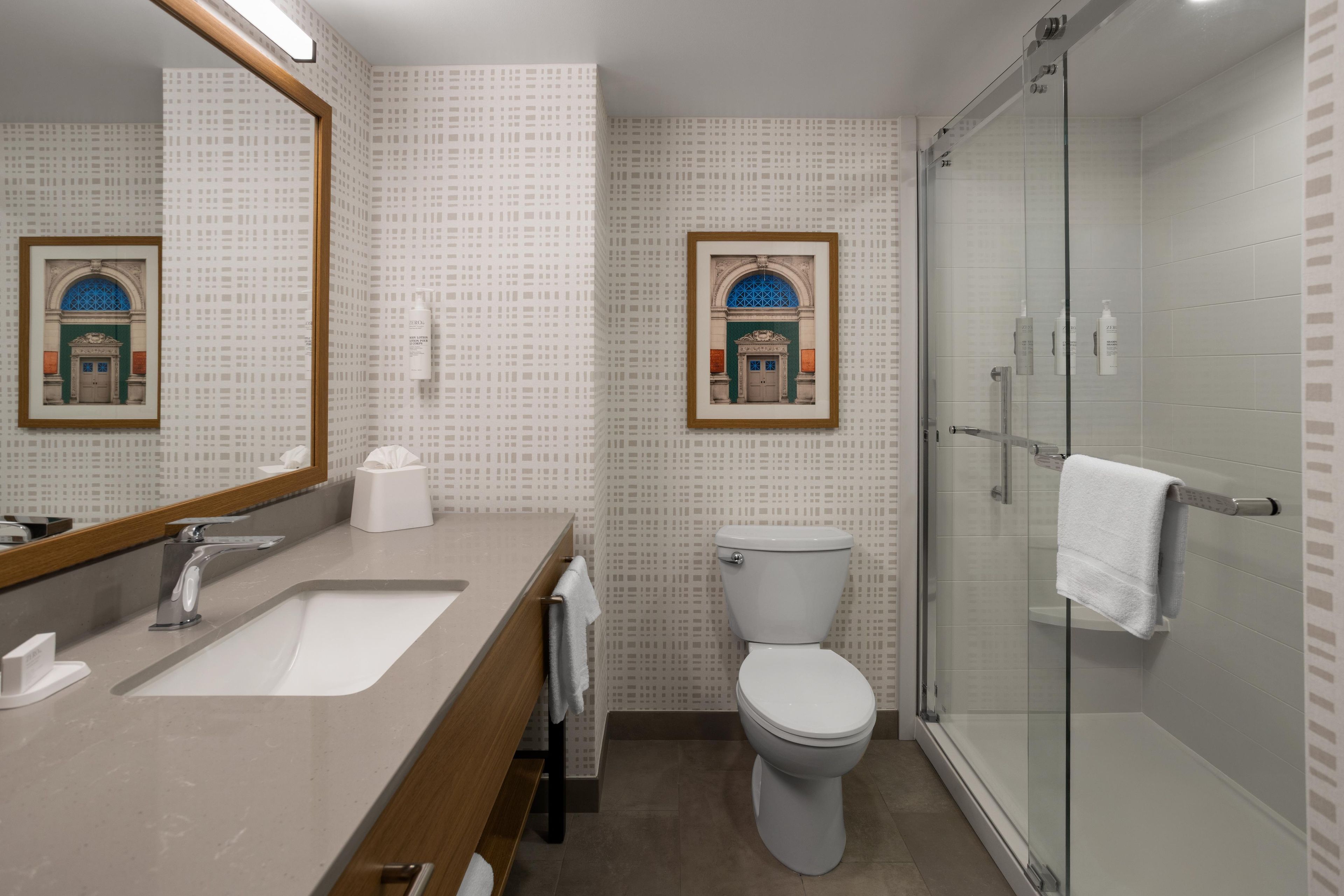 A modern bathroom with a large mirror, a sink, a toilet, and a glass shower enclosure.