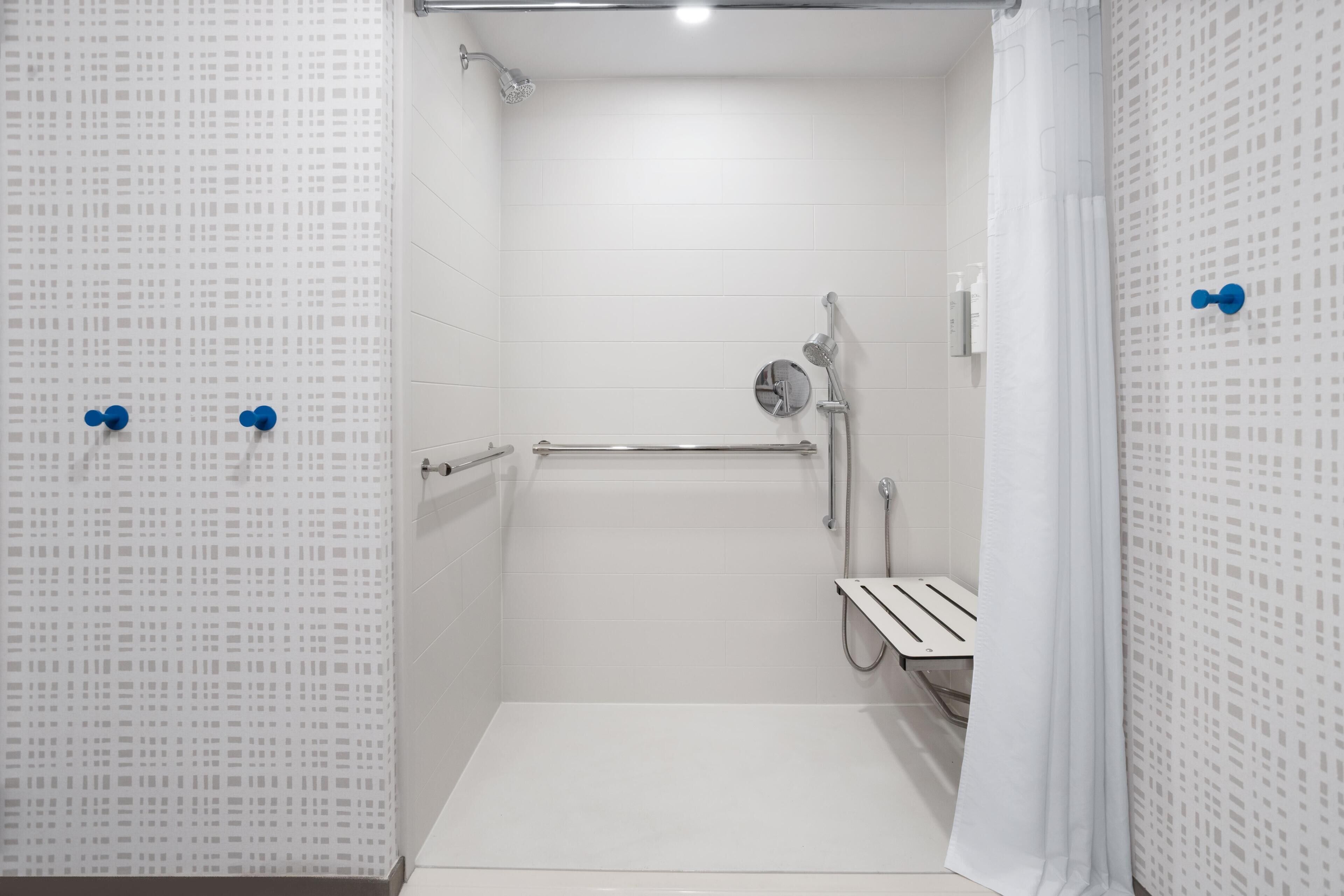 A small, white, tiled shower room with a handheld showerhead, a towel rack, and a shower control panel.