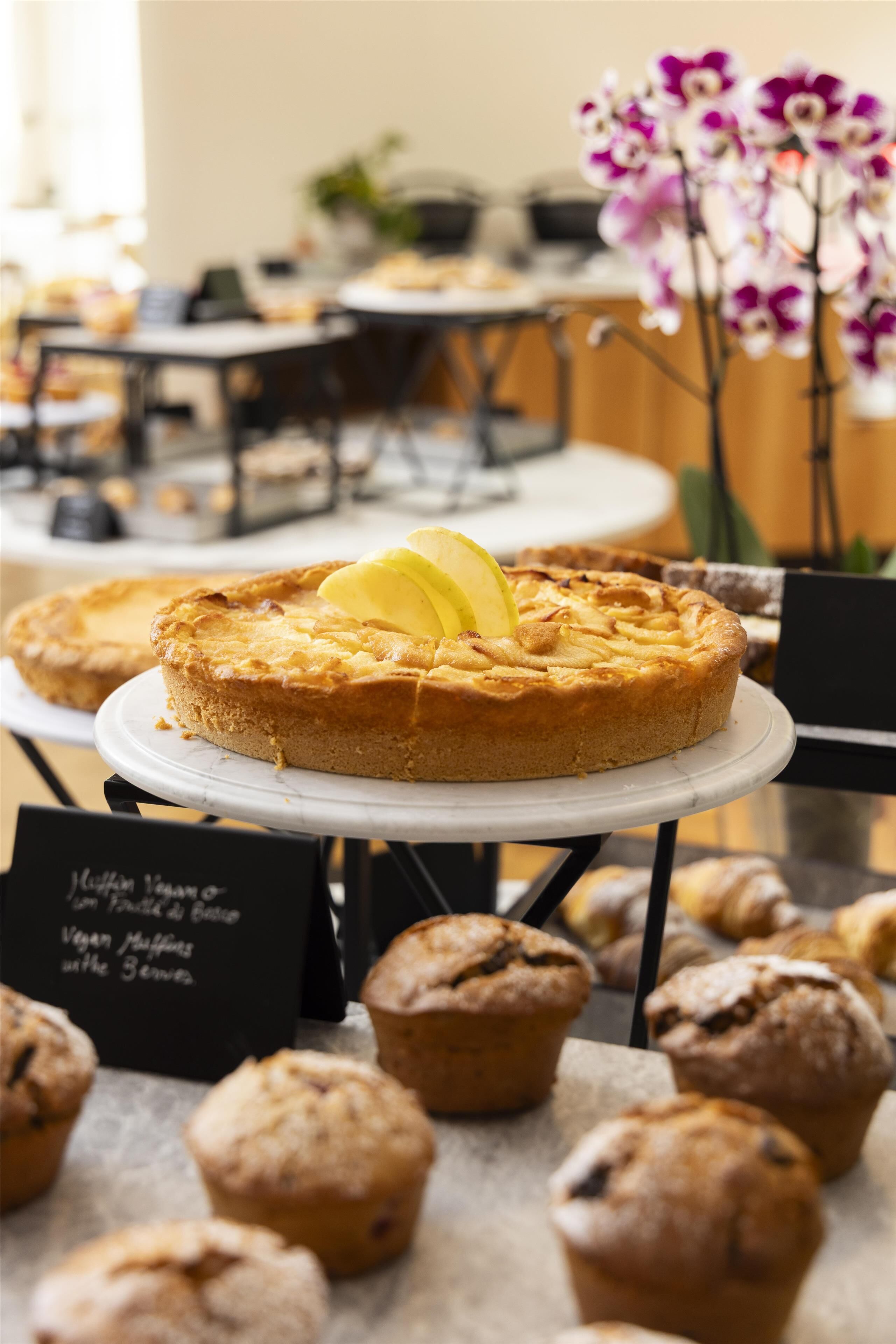 Une table où sont présentés des desserts, notamment un gâteau et des muffins, avec un panneau indiquant les options végétaliennes.